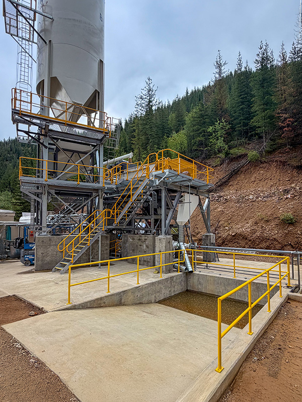 The paste backfill plant includes chisel-nose cement silo, weigh hopper & conveyor for trailings, and twin-shaft mixer / pugmill.